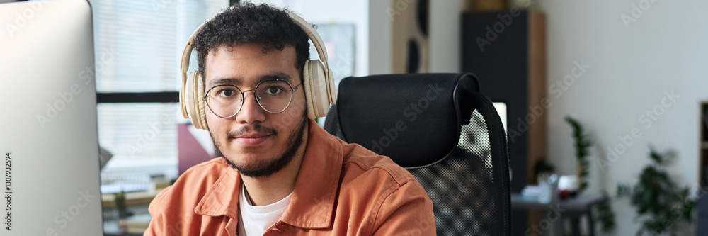 Aufkleber header of young smiling man in eyeglasses and headphones looking at camera during network while sitt