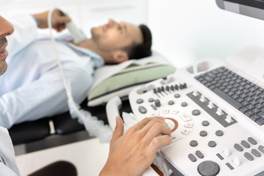 Doctor performing exam to evaluate thyroid function on patient lying down on examination table, close up view to ultrasound machine. Modern medical diagnostics, healthcare technology, patient care