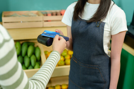 Closeup of digital payment process using contactless credit card in tropical fruit shop between Asian female customer and seller showing seamless technology in small business environment