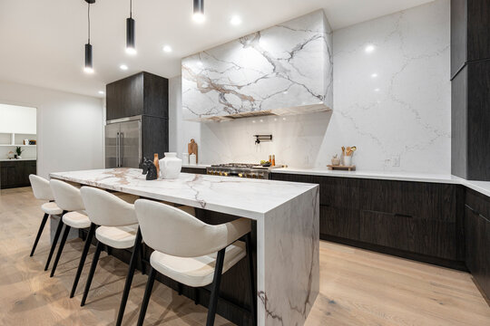 A kitchen with marble countertops, black cabinets, and white chairs
