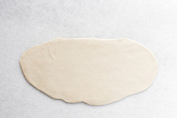 Overhead view of chinese scallion pancake dough being rolled on white countertop, top view of homemade scallion pancakes, process of making cong you bing