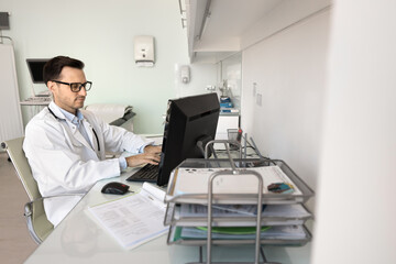 Focused Latin therapist working online using computer in modern workplace, researching medical advancements, updating electronic health records, writing prescriptions, scheduling patient appointments