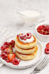 Cottage cheese pancakes with sour cream, strawberries and red currant on white marble background. Traditional russian and ukrainian dish for breakfast syrniki. Side view, close up