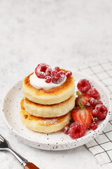 Traditional russian and ukrainian dish for breakfast syrniki. Cottage cheese pancakes with sour cream and fresh berries on white marble background. Side view, close up
