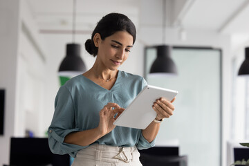 Serious Hispanic executive woman using business application on tablet for project management,...