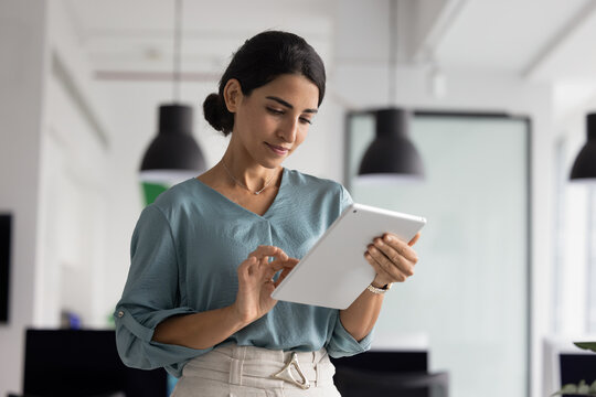 Serious Hispanic executive woman using business application on tablet for project management, working on Internet marketing strategy, typing on screen, browsing social media on digital gadget