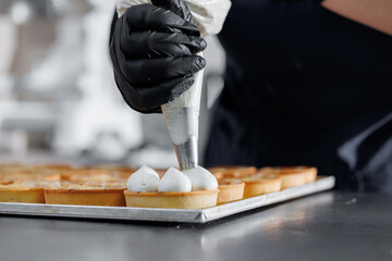 Baker piping cream on tartlets in bakery factory