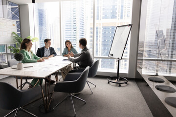 Positive business team sitting at large table in office boardroom interior, discussing company...