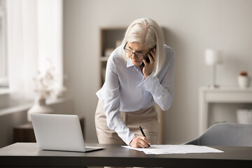 Effective multitasking at workplace. Busy serious senior female entrepreneur executive manager hold...
