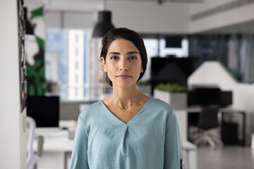 Confident beautiful young Latin businesswoman posing in office space for portrait, looking at...