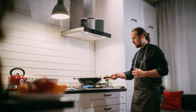 A male cook is cooking at the stove at home in the kitchen