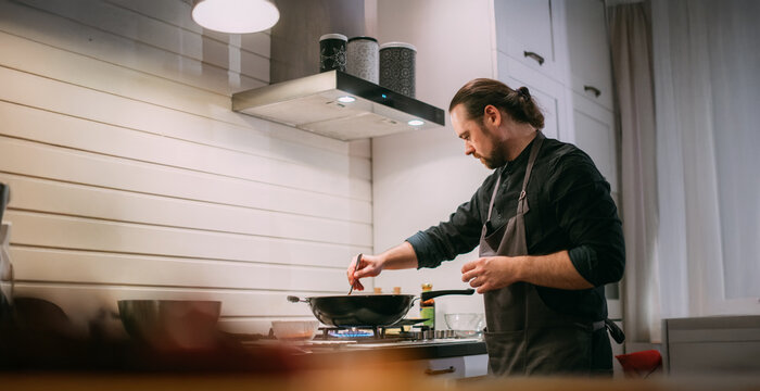 A male cook is cooking at the stove at home in the kitchen