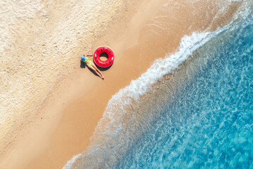 Aerial view of a lying young woman with red swim ring on sandy beach and blue sea at sunset in...