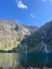  Calm lake nestled beneath steep cliffs mirrors soft clouds and scattered sunbeams