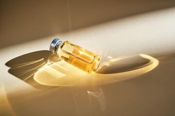 Injection vial with medicinal product in sunlight on beige background. © Marevgenna