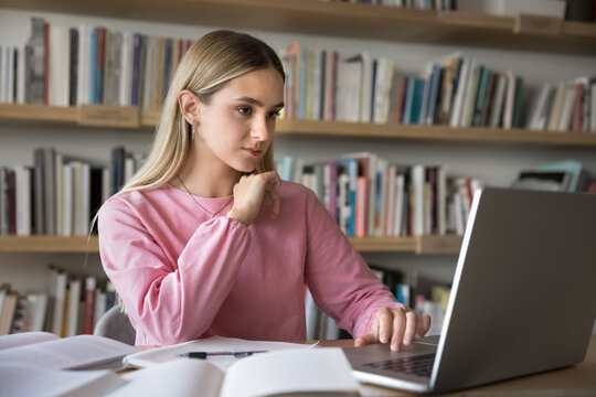 Leaning to search information. Concentrated millennial student girl work with diverse sources of educational material browse scientific websites on notebook pc read paper books take handwritten notes