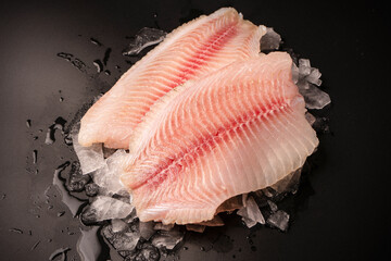 Fresh tilapia fillet on ice on black background