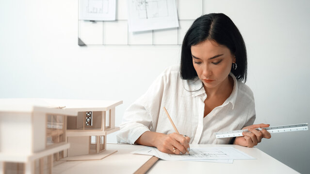 Closeup portrait image of professional young beautiful engineer architect using triangular scale measures house model with focusing at modern office. Business creative design concept. Immaculate.
