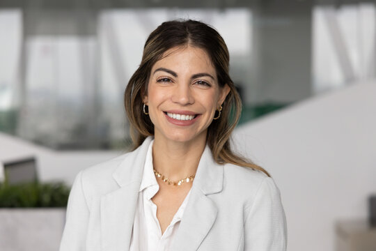 Happy beautiful Hispanic business leader woman posing for head shot with toothy smile, looking at camera, enjoying online conference chat. Confident businesswoman video call screen head shot