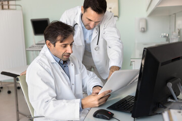 Two cardiologists doctors reviewing medical document, analyzing test results engaged in...