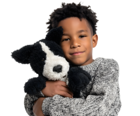 A smiling child with curly hair holds a black and white plush puppy dog toy close to their chest wearing a patterned gray sweater.