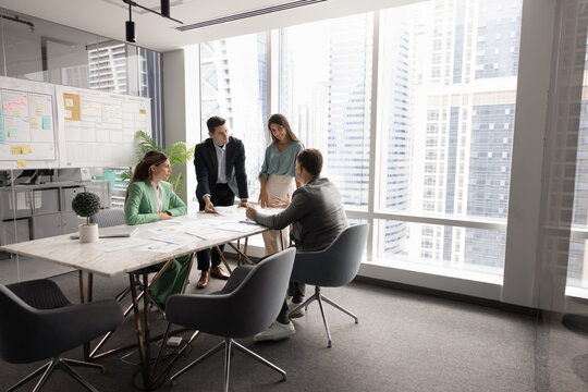 Successful company meeting room space with team of four colleagues, stakeholders, partners sitting at table, working on project together, brainstorming in workspace