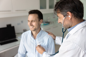 Doctor in white coat using stethoscope listening to male patient heartbeat, placing phonendoscope...