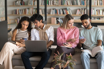 Modern tech in peer learning. Multiracial group high school students zoomers engaged in productive collaborative studying in library share information online using gadgets talk discuss exchange ideas