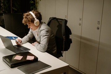 Male intern sitting at a desk and looking at the phone he is holding in front of him, in the...