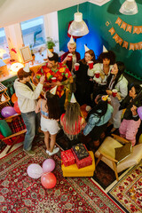 Fototapeta premium A group of ten friends stand at a table and hold cups while talking and looking at each other, at a party