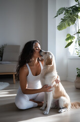 Young pregnant woman wearing white is kissing her golden retriever dog while sitting on the floor at home