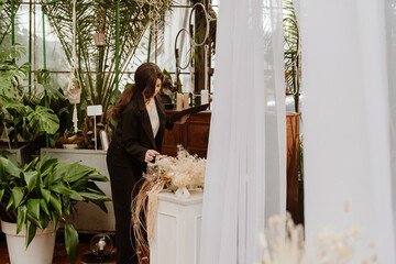 A woman organizer is standing and holding a clipboard while looking at the decorations near which she holds her hand, preparing for the wedding