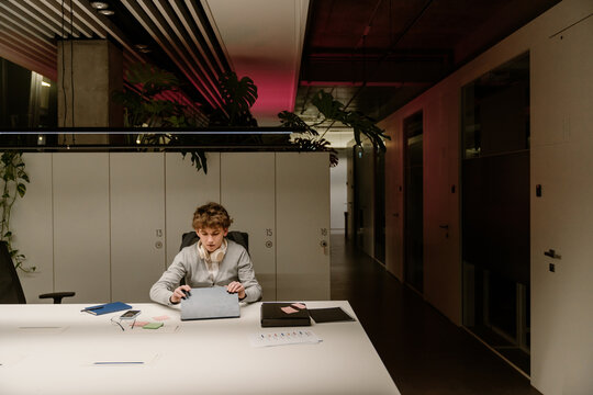 Male intern sitting at a desk and closing a computer tablet, in the office in the evening, during an internship