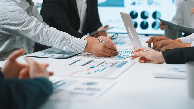 A dynamic business meeting where professionals engage in teamwork to analyze data and review financial reports, fostering collaboration in a modern office setting. SACTR