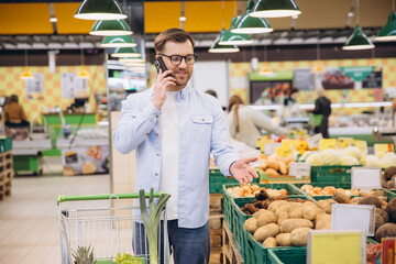 Man talking on smartphone and buying vegetables in supermarket