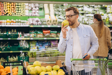 Man smelling a green apple while grocery shopping in a supermarket