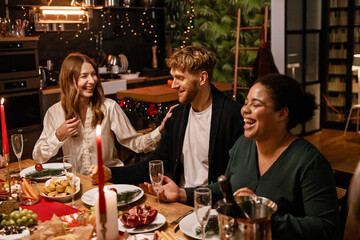 Family and guests sitting at the table and laughing during Christmas dinner