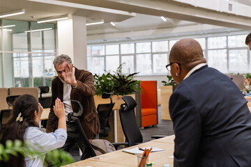 A male employee stands at a desk and watches as a male employee and a female employee give each other a high five, in the hall, before retiring