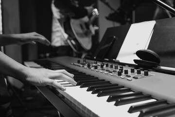 Musician's hands playing a keyboard during worship practice, with a guitarist blurred in the...