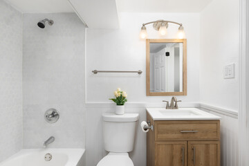 A bathroom with a wood vanity cabinet, white sink, and a shower with a white tub and grey stone hexagon tiles.