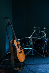 Wooden acoustic guitar on a stand next to a drum set in a music rehearsal or worship space