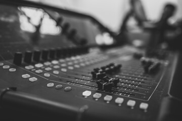 Black and white close-up of an audio mixing console with faders and buttons in a sound studio