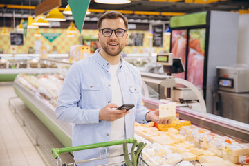 Man using smartphone and buying cheese in supermarket