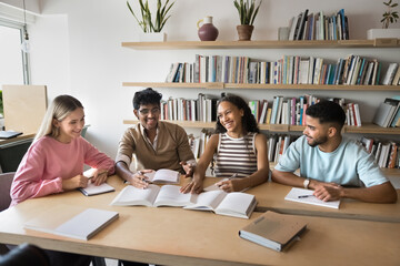 Joyful peer learning. 4 multiethnic teen students sit together at library desk having fun...