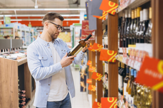 Man choosing wine bottle reading label in supermarket alcohol section