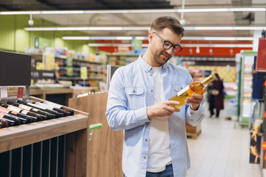 Man choosing white wine bottle reading label in supermarket
