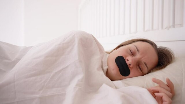 Woman Sleeping Peacefully with Mouth Taped Shut in Bright Bedroom Covered in White Blanket for Daytime Sleep Health Concept