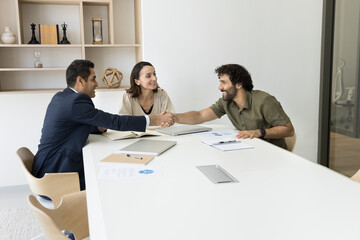 Three businesspeople gather at conference table in office, finish negotiation, formal meeting with handshake, congratulate each other with productive outcome, making agreement, establish collaboration
