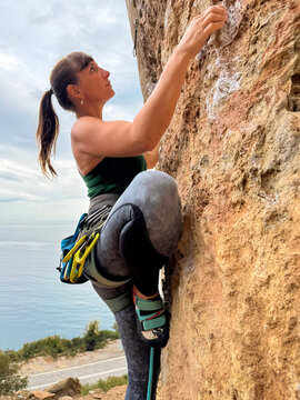 CLOSE UP, PORTRAIT: Rock climber tackles vertical limestone wall in Leonidio, Greece. Equipped with climbing gear and focused on her next hold, she demonstrates strength, technique, and determination.
