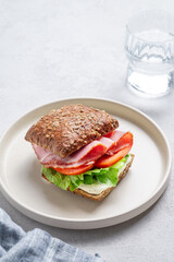 Toast sandwich made of grain bread with prosciutto, cheese, tomatoes, lettuce and sauce on a plate